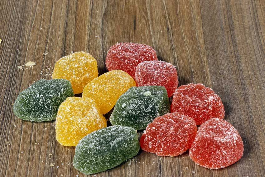 Colorful sugared cannabis gummies in green, yellow, and red on a wood table. Colorful sugared cannabis gummies in green, yellow, and red on a wood table.